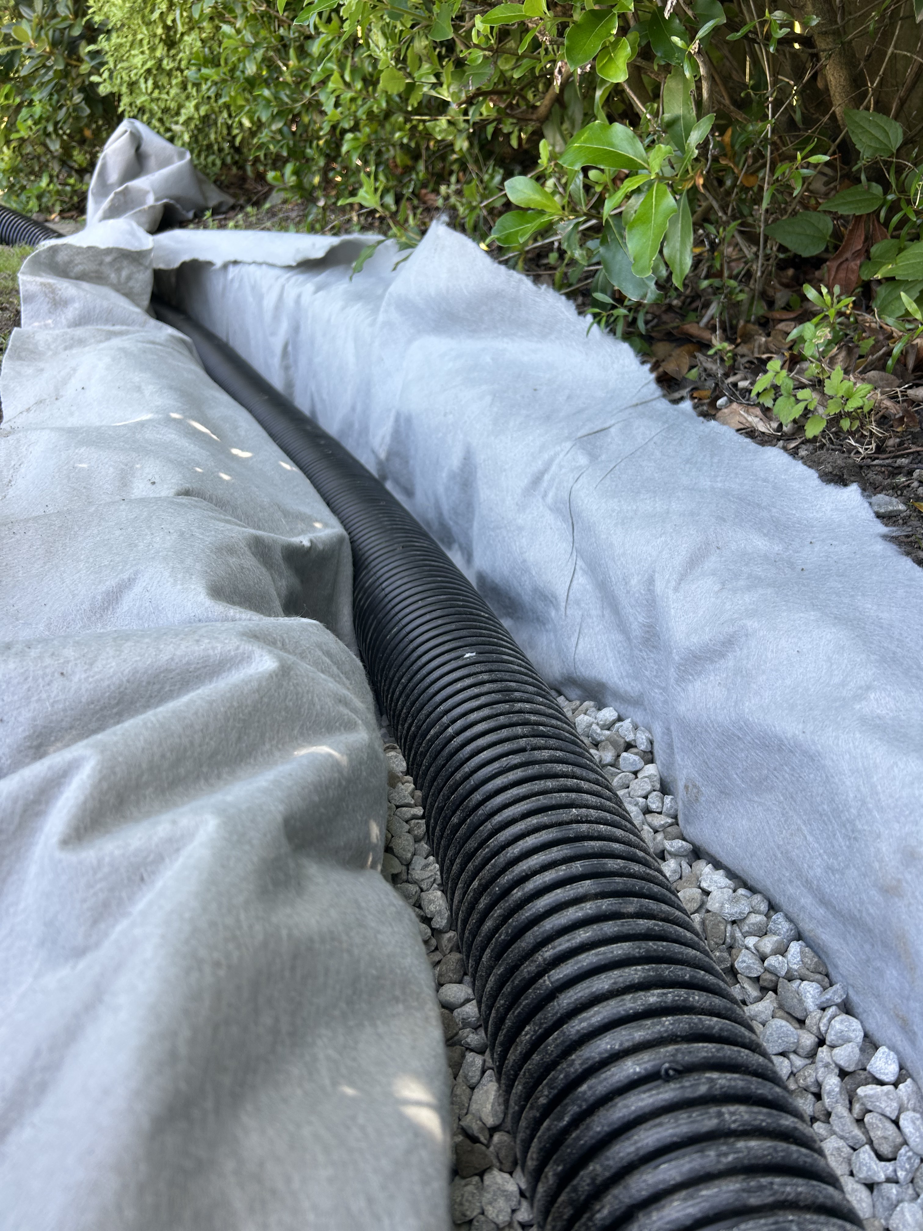 French drain installation — perforated corrugated pipe laid on gravel and wrapped in geotextile fabric